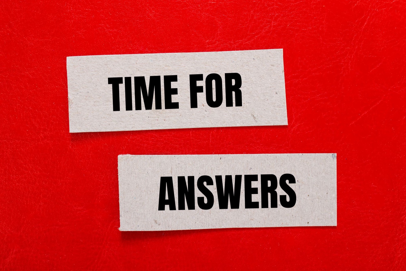 Two torn strips of gray cardboard on a bright red leather background, printed in black capital letters: TIME FOR, and below it, ANSWERS.