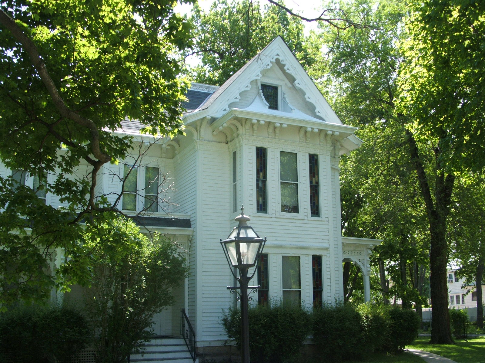 The Harry S. Truman home in Independence, Missouri — a white Victorian house with a wraparound porch, seen from the street through the trees.