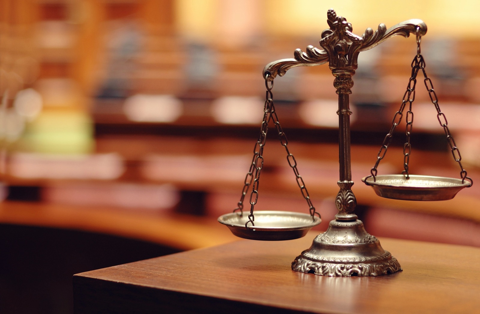 A decorative bronze scales of justice standing on a wooden table in an empty courtroom.